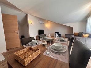 Un coin repas avec une table en bois dressée pour quatre personnes, un panier en osier et un canapé gris en arriÚre-plan.
