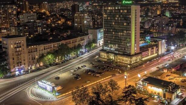 Un hotel moderno de gran altura, con varios pisos y un llamativo letrero verde en la parte superior.