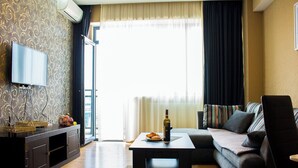 Una sala de estar con sofá, mesa de centro, televisor y ventana con cortinas.