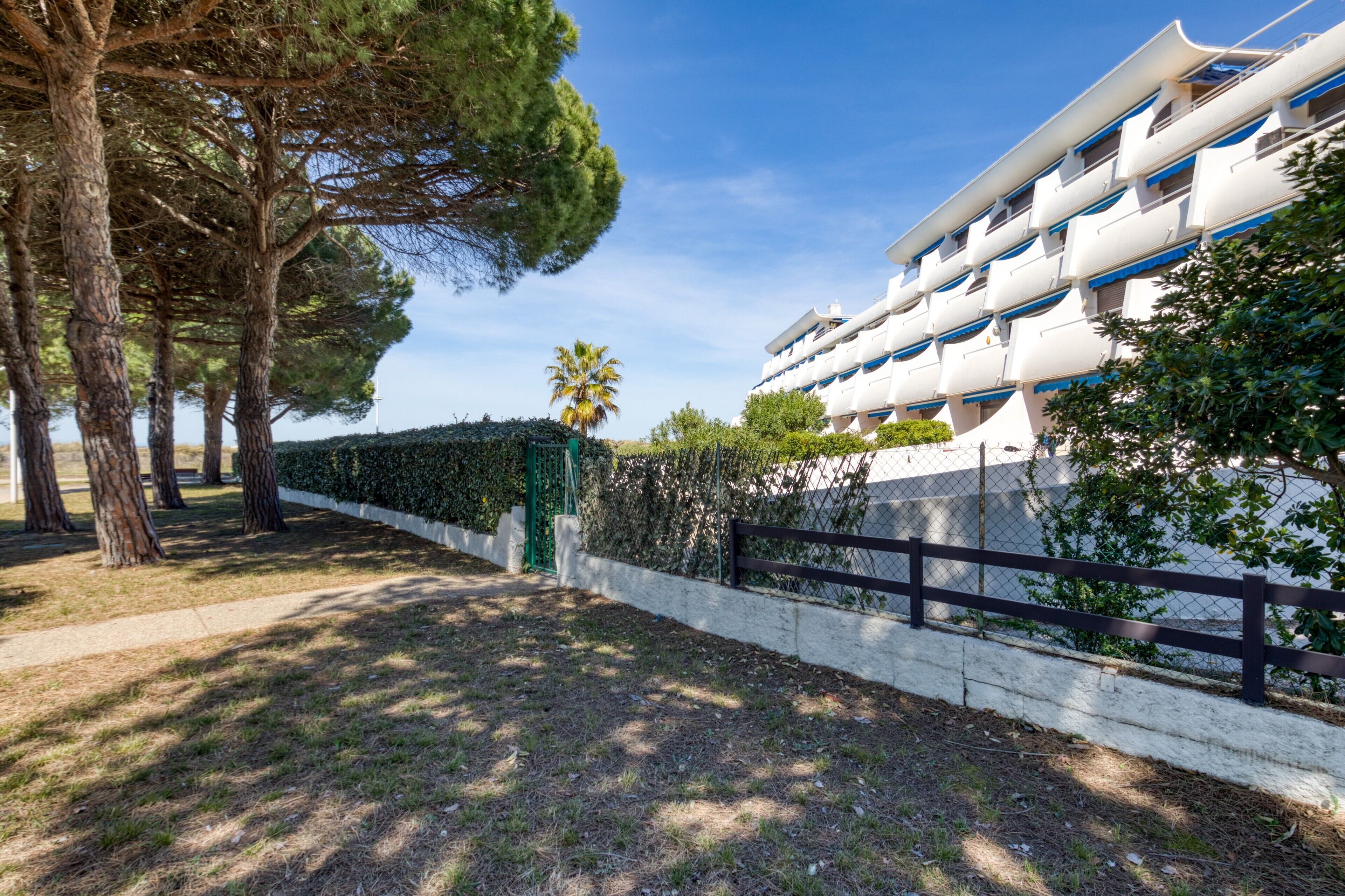 Un hotel moderno con fachada blanca, varios balcones y un jardín bien cuidado con árboles y setos.