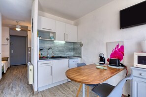 A compact kitchen with white cabinets, a wooden dining table, a microwave, and a television. - Bright Sea View Studio with Balcony and Direct Beach Access (Le Grau-du-Roi)