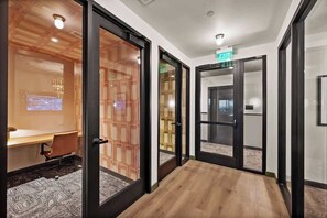 A hallway with glass doors, a wooden floor, and a conference room with a projector screen. - Downtown Salt Lake City Luxury Retreat - Pool, Sauna, and Parking (Salt Lake City)