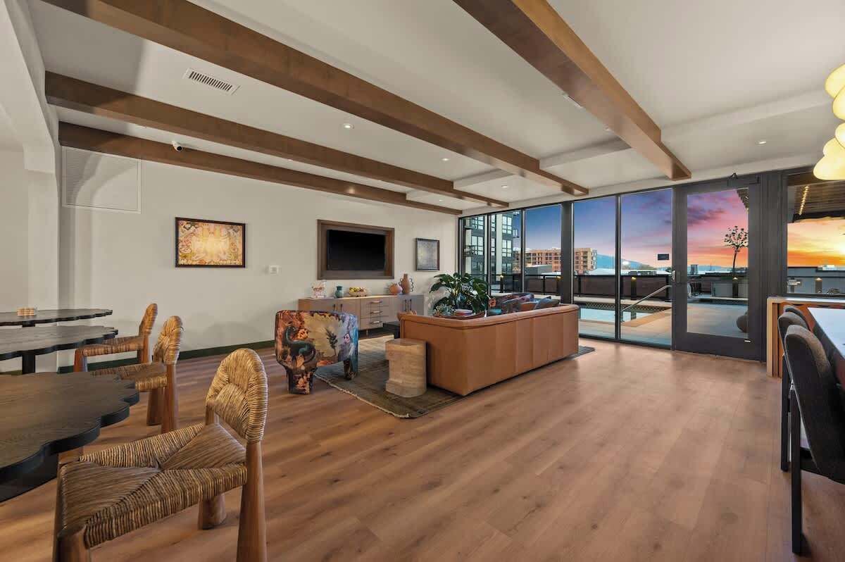 A spacious living area with a large window, a dining table, and a sofa.
