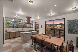 A modern kitchen with a large island, a dining area with patterned chairs, and a city view through large windows. - Elevated Downtown SLC Stay - Pool + Sauna Retreat (Salt Lake City)