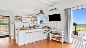A modern kitchen with wooden countertops, white bar stools, and a large window overlooking a scenic view.