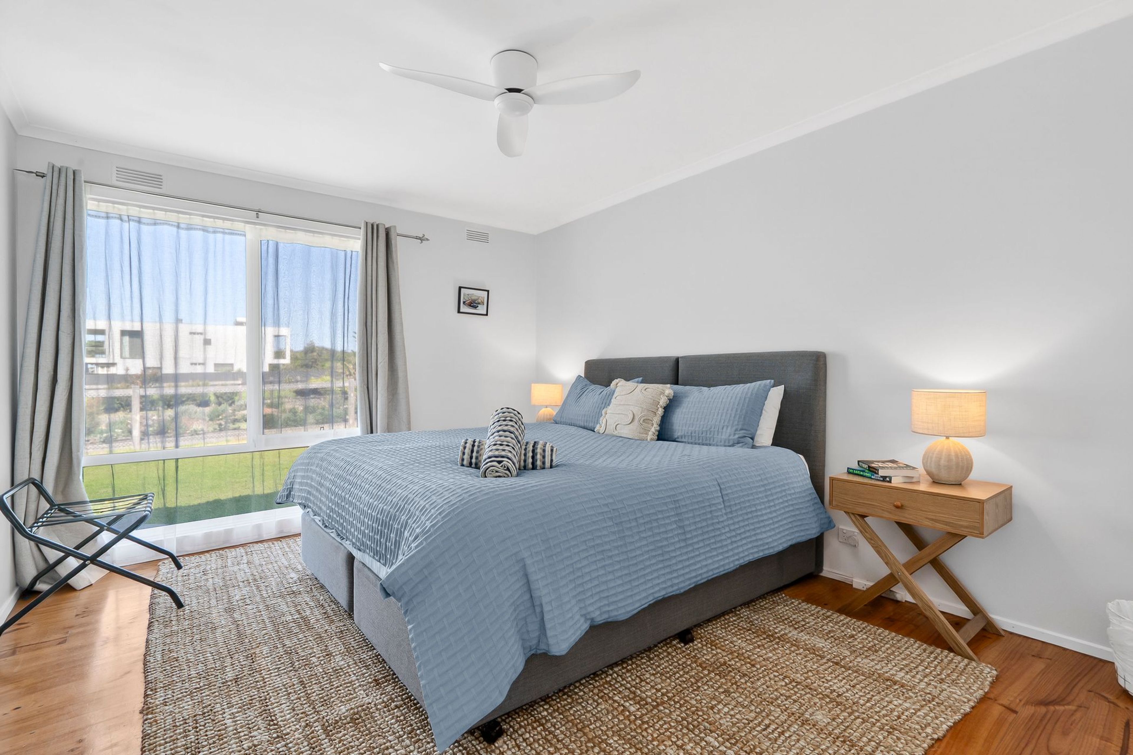 A bedroom with a bed, a nightstand, a chair, a window, and a ceiling fan.