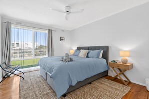 Ein Schlafzimmer mit einem Bett, einem Nachttisch, einem Stuhl, einem Fenster und einem Deckenventilator.