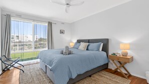 A bedroom with a bed, a nightstand, a lamp, a chair, and a view of the outside. - Beachfront Apartment @ Apollo (Apollo Bay)