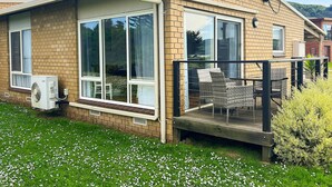 Una casa de un piso con fachada de ladrillo, ventanas grandes y un porche cubierto con mobiliario exterior.