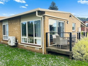 A single-story house with a brick exterior, large windows, and a covered porch with outdoor furniture. - Beachfront Apartment at Apollo (Apollo Bay)