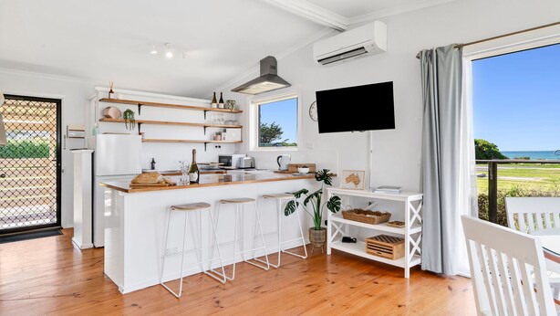 Una cocina moderna con una isla central, taburetes de bar, un televisor de pantalla plana y vistas al exterior.