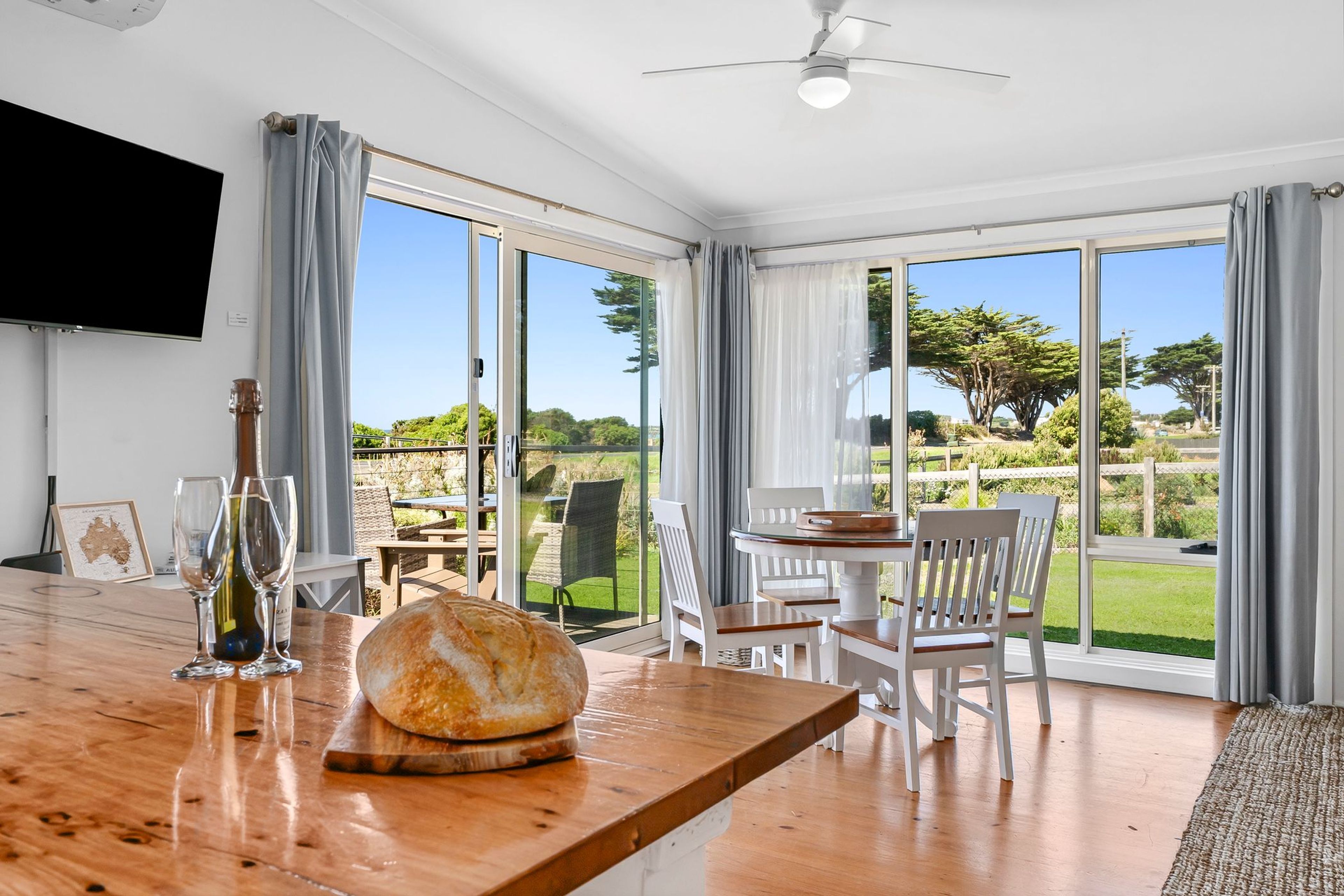 A dining area with a wooden table, chairs, and a view of the outdoors through large glass doors.