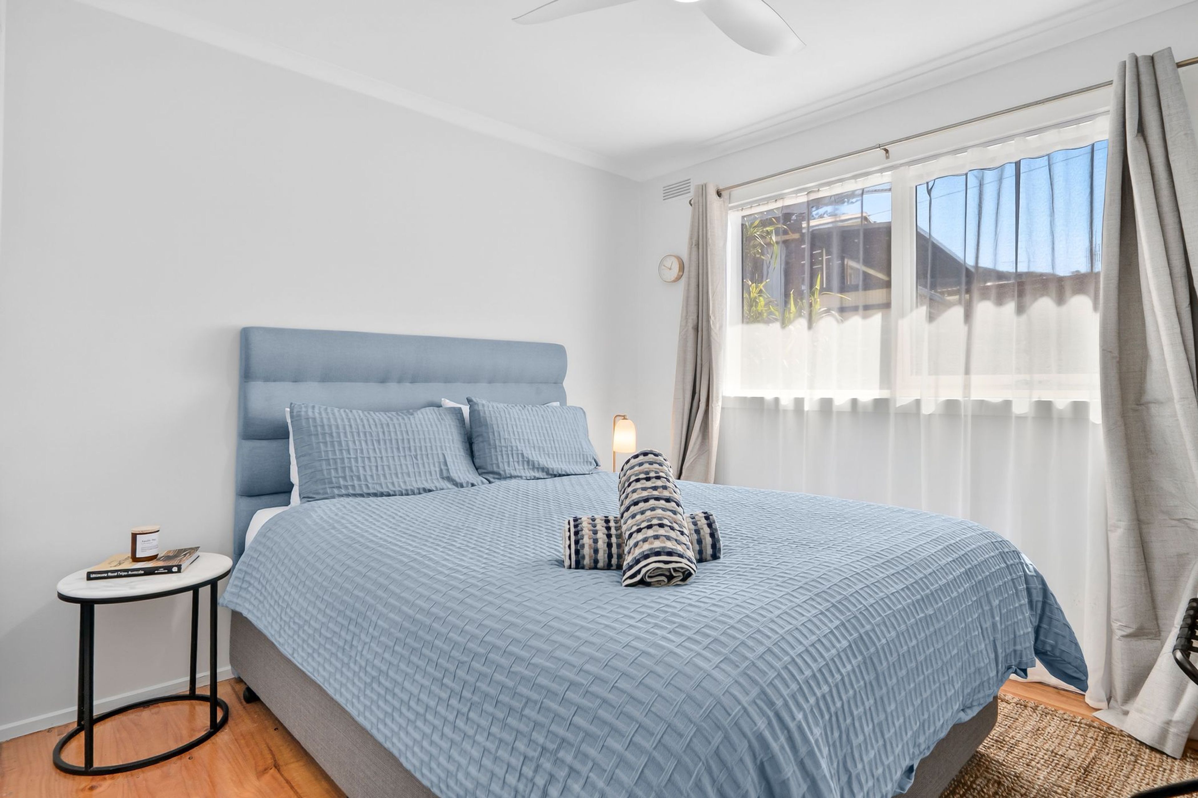 Une chambre à coucher avec un lit, une table de chevet, une lampe et une fenêtre avec des rideaux.