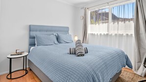 Un dormitorio con cama, mesita de noche, lámpara y ventana con cortinas.