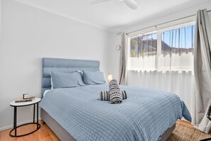 A bedroom with a bed, a bedside table, a lamp, and a window with curtains. - Beachfront Apartment at Apollo (Apollo Bay)