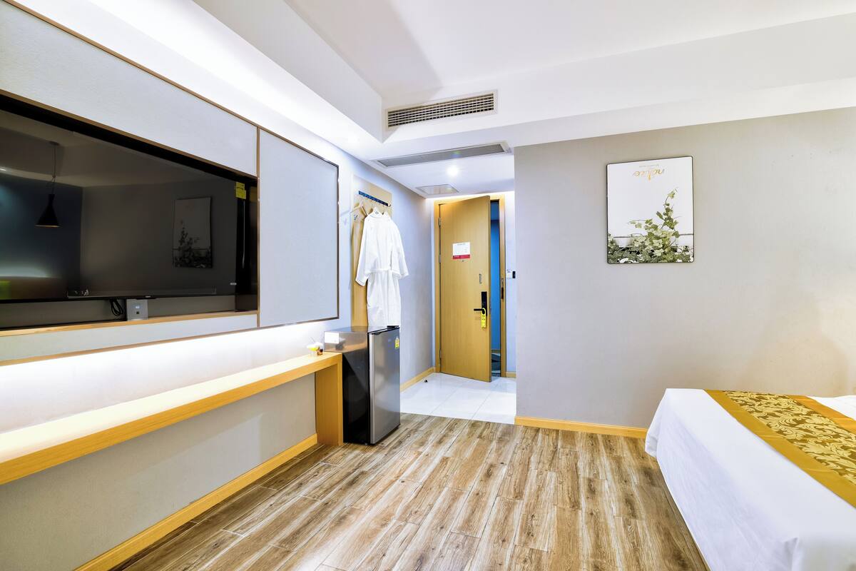 Een hotelkamer met een bed, televisie, bureau, koelkast, spiegel, deur en een aan de muur hangend schilderij.