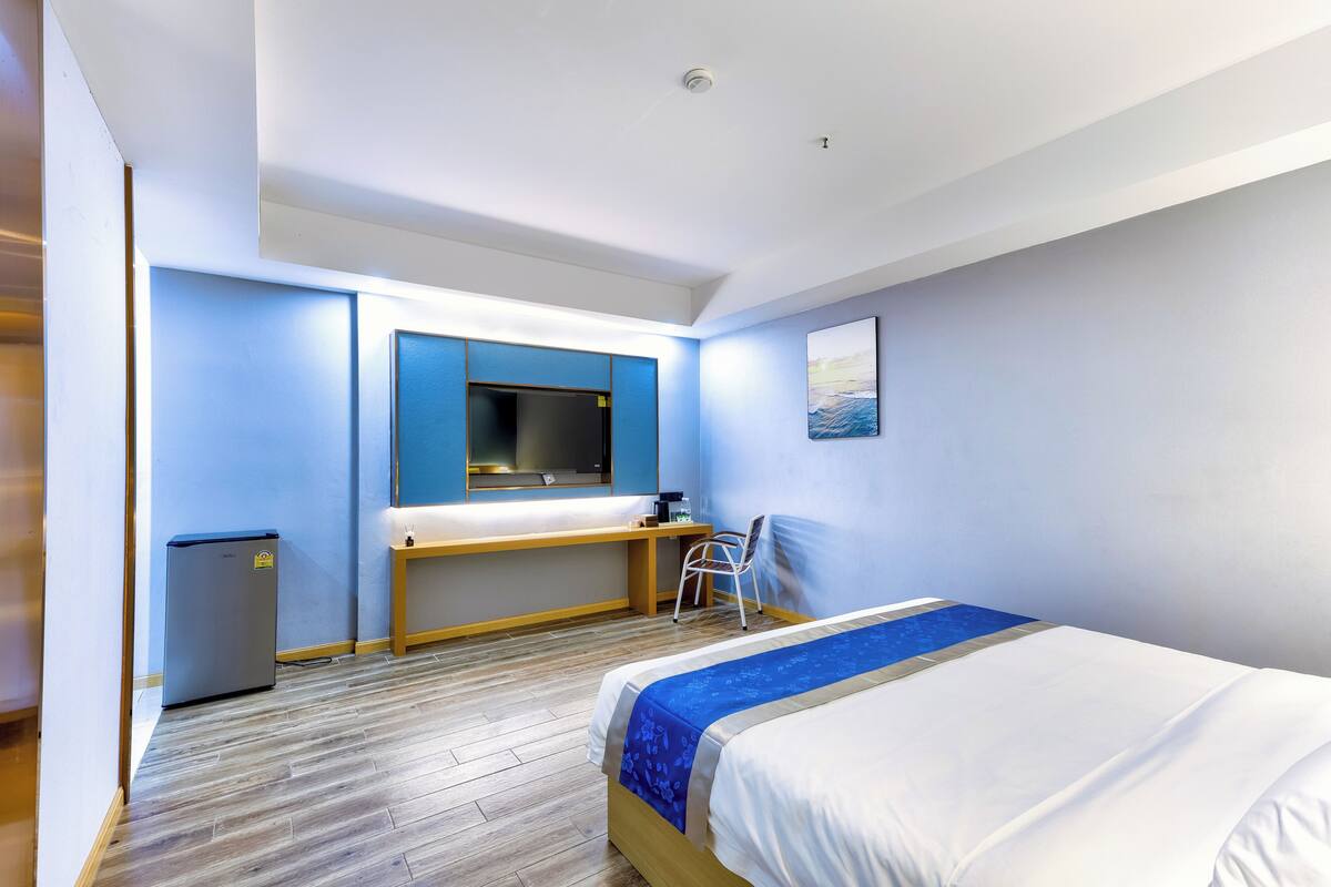 Een hotelkamer met een bed, een bureau, een stoel, een kleine koelkast en een foto aan de muur.
