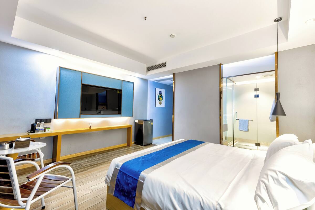 Een hotelkamer met een bed, een bureau, een stoel, een kleine koelkast, een spiegel en een raam.