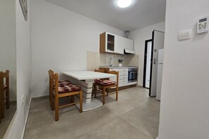 A compact kitchen with a white table and chairs, a built-in oven, and a refrigerator. - Coastal Bungalow for 5 in Zaton (Zaton)