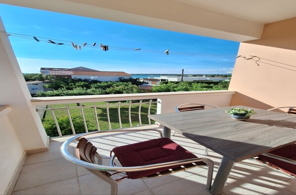A balcony with a table and chairs, a view of buildings and greenery, and a clear sky. - Coastal Bungalow for 5 in Zaton (Zaton)