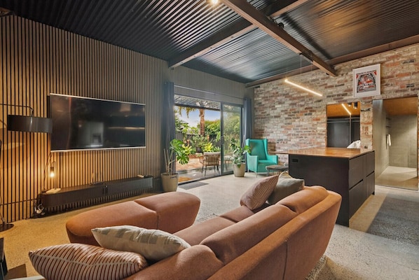 A modern living room with a sofa, TV, and a brick wall. - The Midnight Hideaway (North Beach)