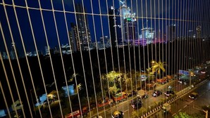 Une vue nocturne sur une ville, avec de hauts immeubles, une rue animée où circulent des véhicules et un pont aux lignes verticales.