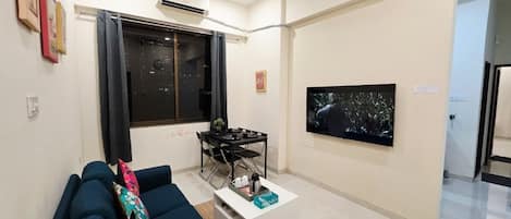 A living room with a sofa, a coffee table, a TV, and a dining area.