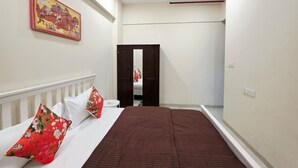Une chambre à coucher avec un lit, des oreillers, une table de chevet, un miroir et une porte donnant sur une autre pièce.