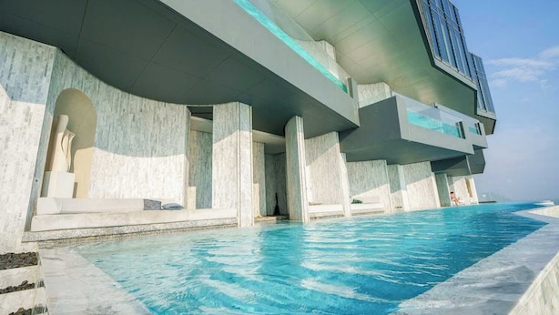 A modern hotel with a large infinity pool, a poolside lounge area, and a view of the ocean. - Luxury 2BR Sea View Apartment with Private Lift and Free Parking (Pattaya)