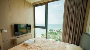 A hotel room with a bed, a TV, a window with a view of the sea, and a curtain. - Luxury 2BR Sea View Apartment with Private Lift and Free Parking (Pattaya)