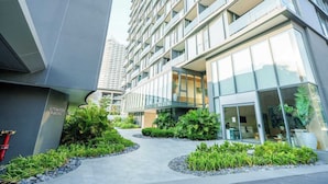 A modern building with a glass facade, a landscaped courtyard with plants, and a sign indicating automated parking. - Luxury 2BR Sea View Apartment with Private Lift and Free Parking (Pattaya)