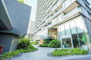 A modern building with a glass facade, a landscaped courtyard with plants, and a sign indicating automated parking. - Luxury 2BR Sea View Apartment with Private Lift and Free Parking (Pattaya)