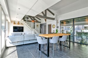 Eine moderne Küche mit einer zentralen Kochinsel, einer Treppe und einem Wohnbereich mit Sofa und Fernseher.