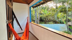 Un pasillo con techo de madera, una hamaca, un ventanal con vistas a la vegetación y una piscina.