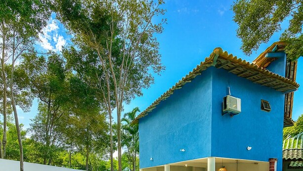 Un área de piscina con sillones de descanso, un edificio azul con techo de tejas y un cielo despejado.