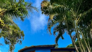 Un edificio de dos pisos con fachada azul, techo de tejas y un pequeño porche delantero con una hamaca.