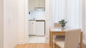 A compact kitchen with white cabinets, a small refrigerator, and a dining area with a table and chair. - Suite Élégance at Montparnasse (Paris)