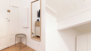 A room with a white door, a round table, a mirror, and a white wall with a decorative molding. - Suite Élégance at Montparnasse (Paris)