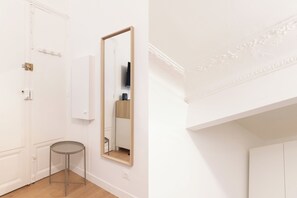 A room with a white door, a round table, a mirror, and a white wall with a decorative molding. - Suite Élégance at Montparnasse (Paris)