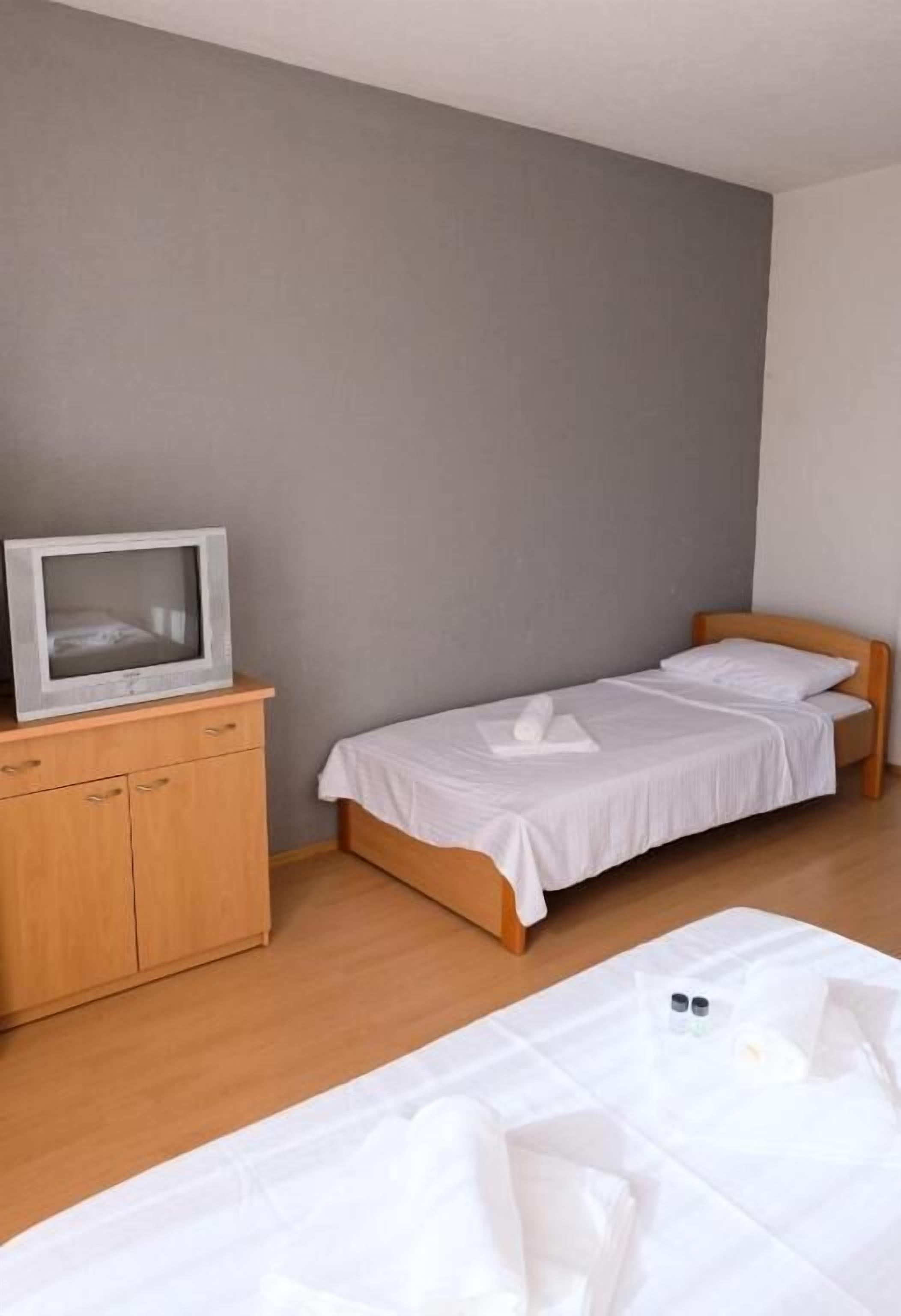 A small, single-bed room with a wooden cabinet and a television on top.
