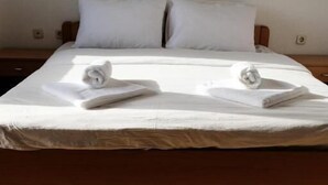 A neatly made bed with white linens and towels, a wooden headboard, and a plain wall. - Ariston Hotel (Misleshevo)