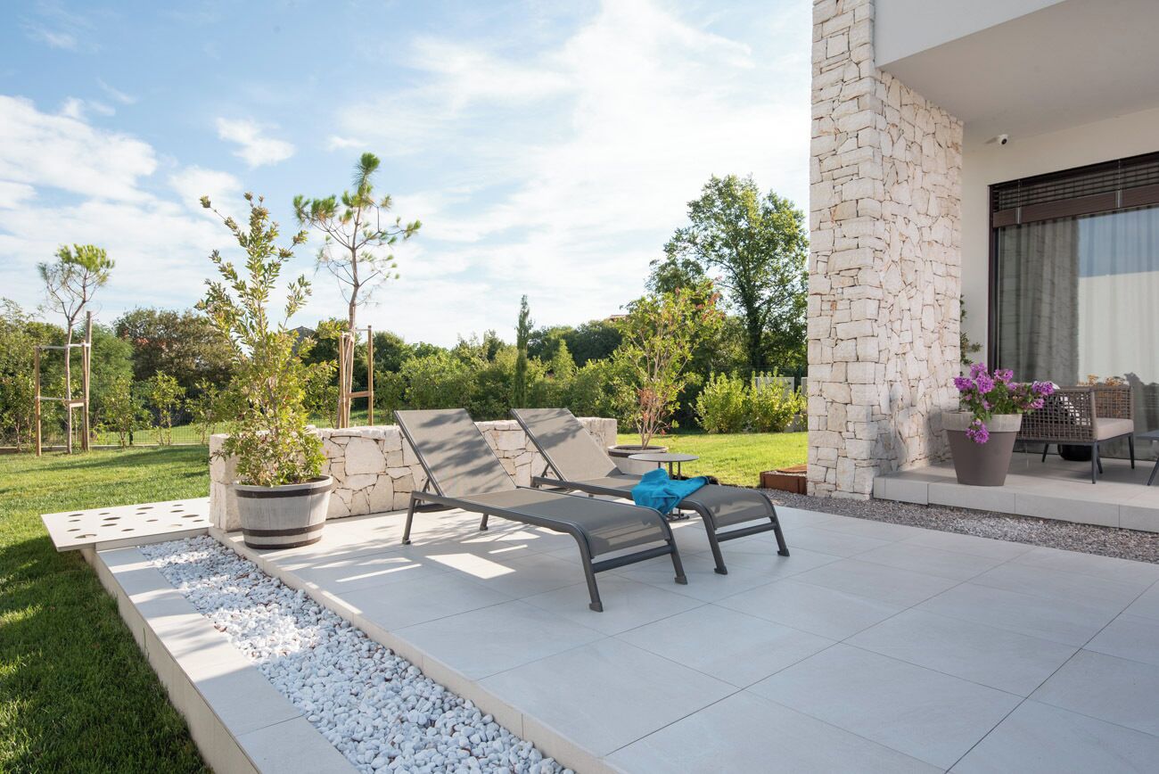 Eine moderne Terrassenanlage mit Lounge-Möbeln, einer Steinmauer und einem Garten.