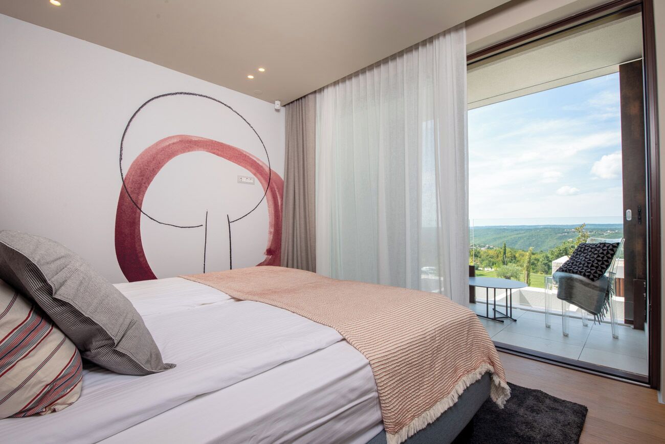 Ein Schlafzimmer mit einem großen Bett, Blick ins Freie und einem Balkon mit Tisch und Stühlen.