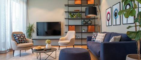 A modern living room with a flat-screen TV, two armchairs, a sofa, a coffee table, and a bookshelf.