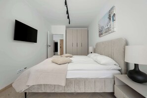 A modern bedroom with a bed, bedside table, lamp, and a wall-mounted TV. - Modern Apartment | Parking | View of the Oder River (Wrocław)