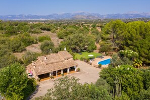 A villa with a tiled roof, a swimming pool, and a tennis court surrounded by greenery and mountains in the background. - 4 person villa with private pool (Llubi)