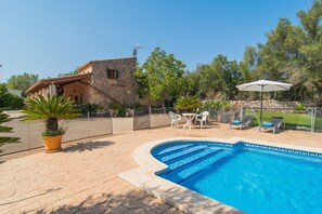 A swimming pool with lounge chairs and a table, surrounded by a stone building and greenery. - 4 person villa with private pool (Llubi)