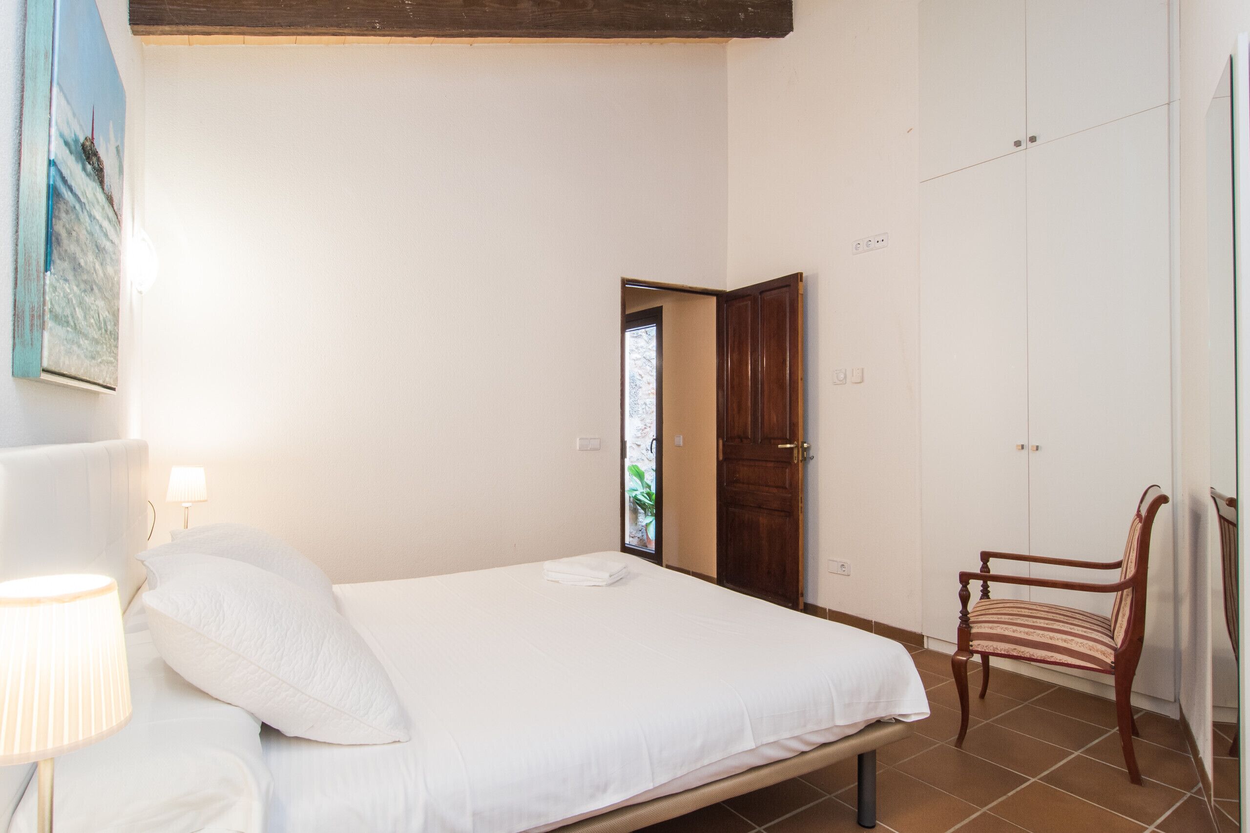 A bedroom with a bed, a chair, a door, and a wall-mounted lamp.