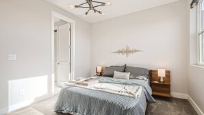 Quarto com cama, mesas de cabeceira, uma obra de arte na parede e uma porta.