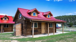 A wooden cabin with a red roof, a porch, and a small attached structure. - Red Canyon Village (Panguitch)